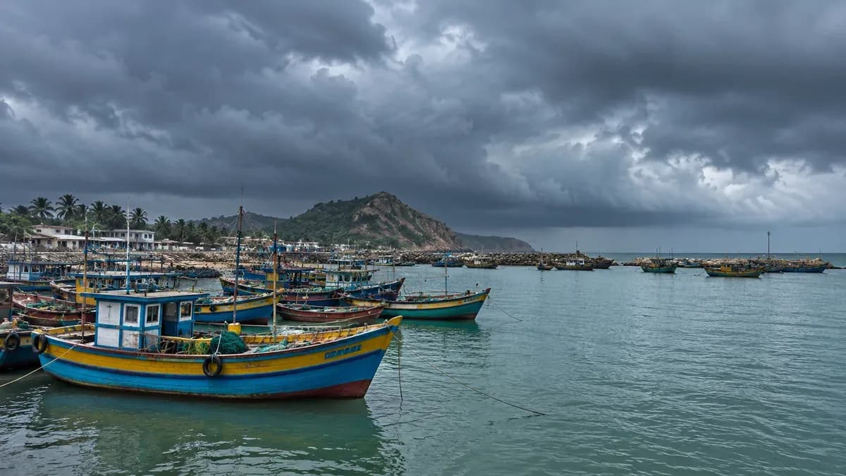 A generic Andhra-style Indian coastline before a storm, fishing boats safely moored in a small harbour, heavy grey cloud bank, natural muted sea green and blue, no destruction, no actual cyclone depiction.